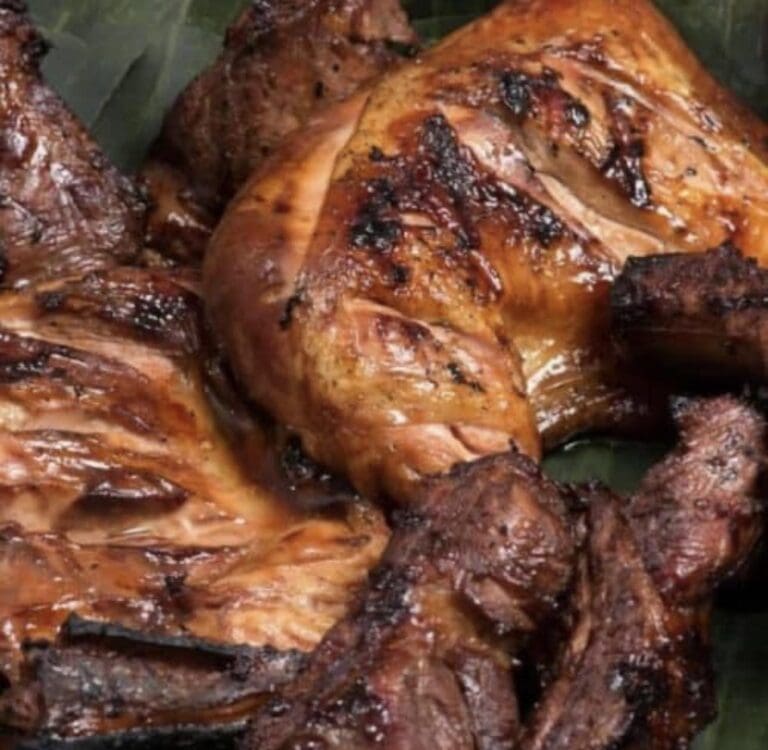 Grilled whole chicken with charred skin and seasoning, displayed on a dark surface, representing local cuisine in Roatan, Honduras.