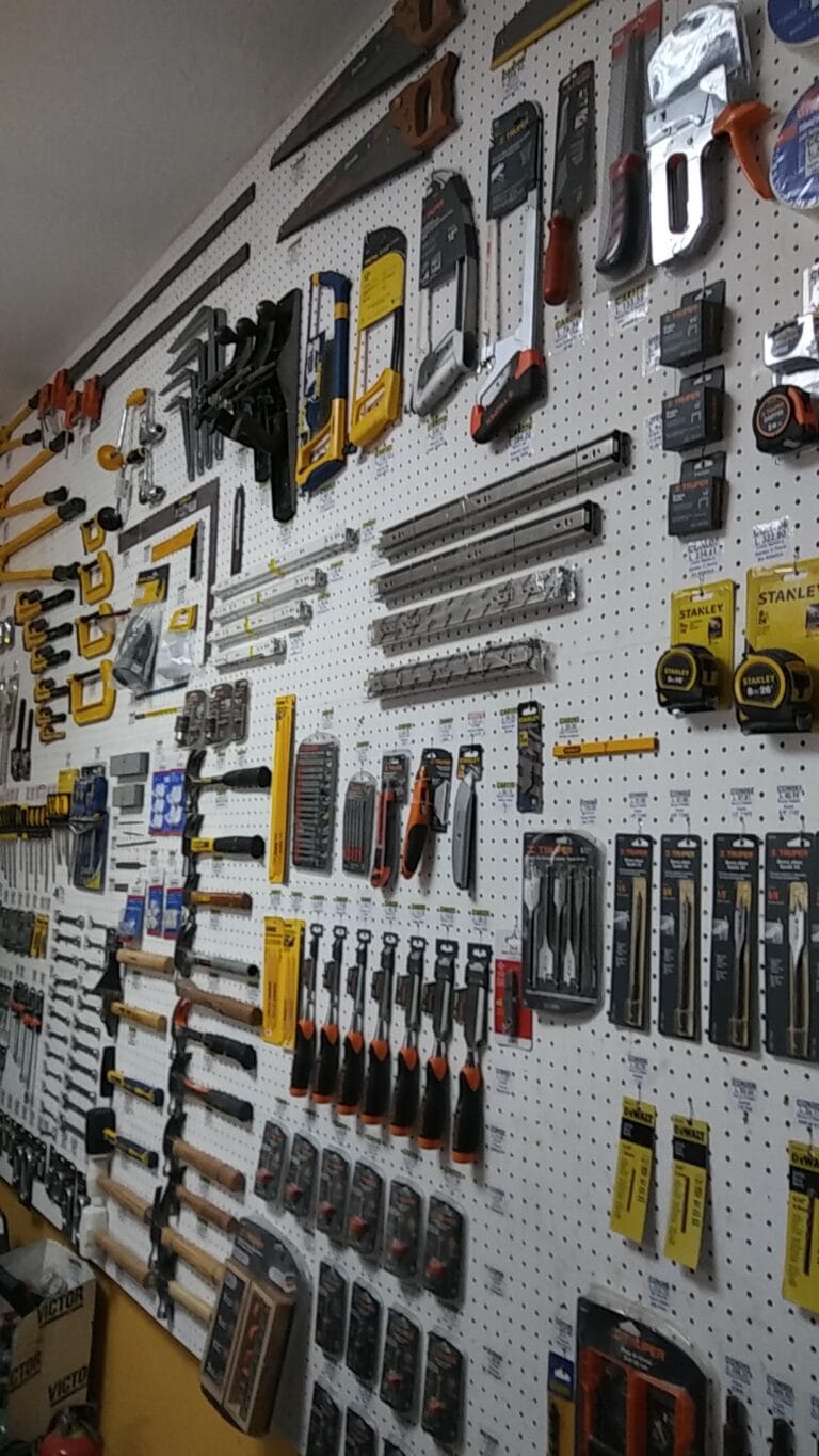 A variety of hand tools, including saws, hammers, screwdrivers, and measuring tapes, are displayed on a pegboard wall inside a hardware store in Roatan, Honduras.