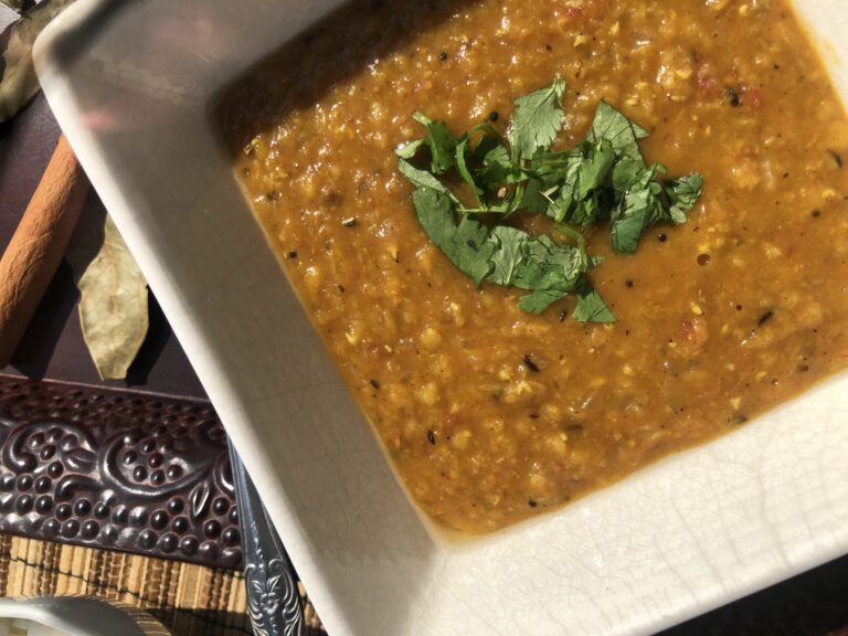 A bowl of traditional Honduran bean and vegetable soup garnished with fresh cilantro, served in a white dish on a table in Roatan, Honduras.