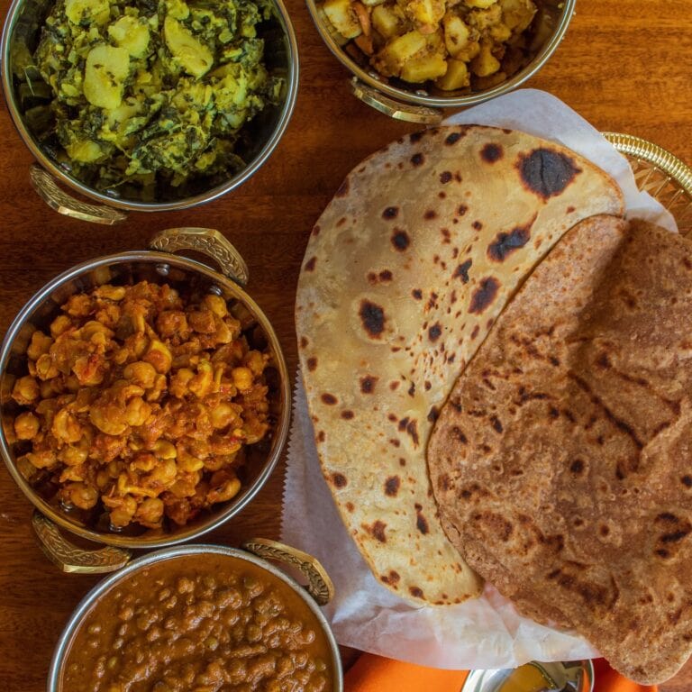 A traditional Honduran meal featuring large tortillas served with five bowls of various stews and side dishes on a wooden table in Roatan.