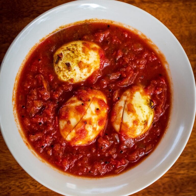 A bowl of huevos rancheros topped with tomato sauce, served on a white dish placed on a wooden surface in Roatan, Honduras.