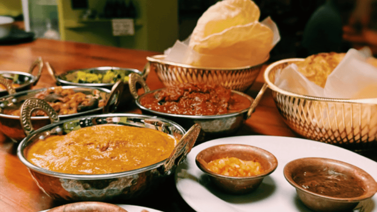 An assortment of traditional Honduran and Roatan dishes, including various stews, sauces, and bread, is displayed on a wooden table in a restaurant setting in Roatan, Honduras.
