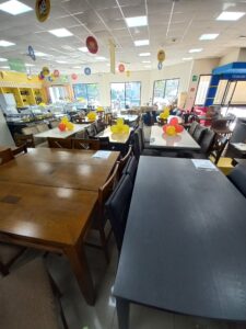 A brightly lit retail store in Roatan, Honduras, featuring tables decorated with yellow and red balloons, shelves stocked with appliances, and signage indicating various product sections.