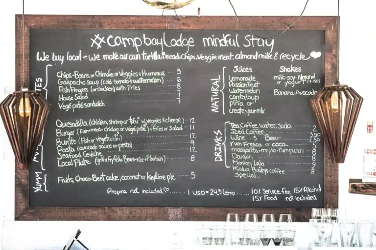 A black chalkboard menu at a Roatan, Honduras restaurant displaying various food and drink options with handwritten white chalk text and two wooden lantern-style light fixtures on each side.