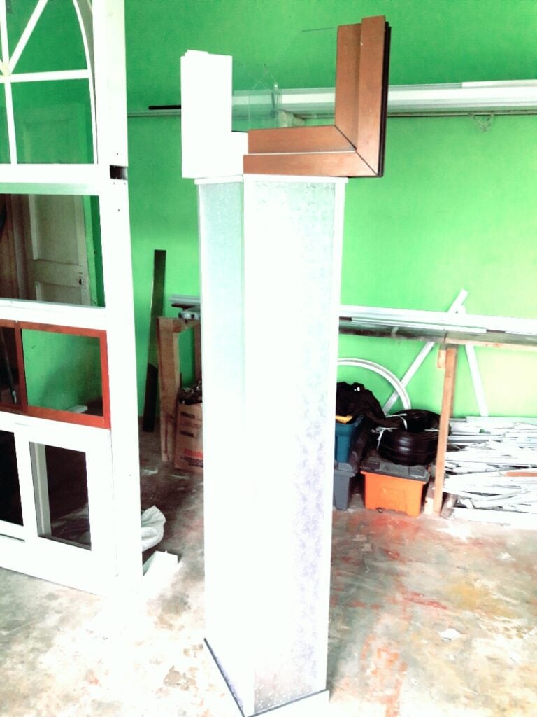 A partially built interior space with bright green walls, construction materials, and tools scattered on the floor, with a white and wooden display case or shelving unit, indicating ongoing renovation in Roatan, Honduras.