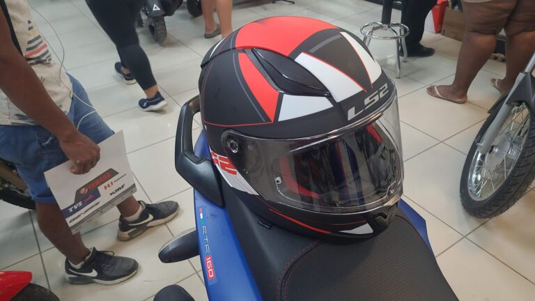 A black, red, and white motorcycle helmet displayed on a seat inside a store in Roatan, Honduras, with people around inspecting various items.