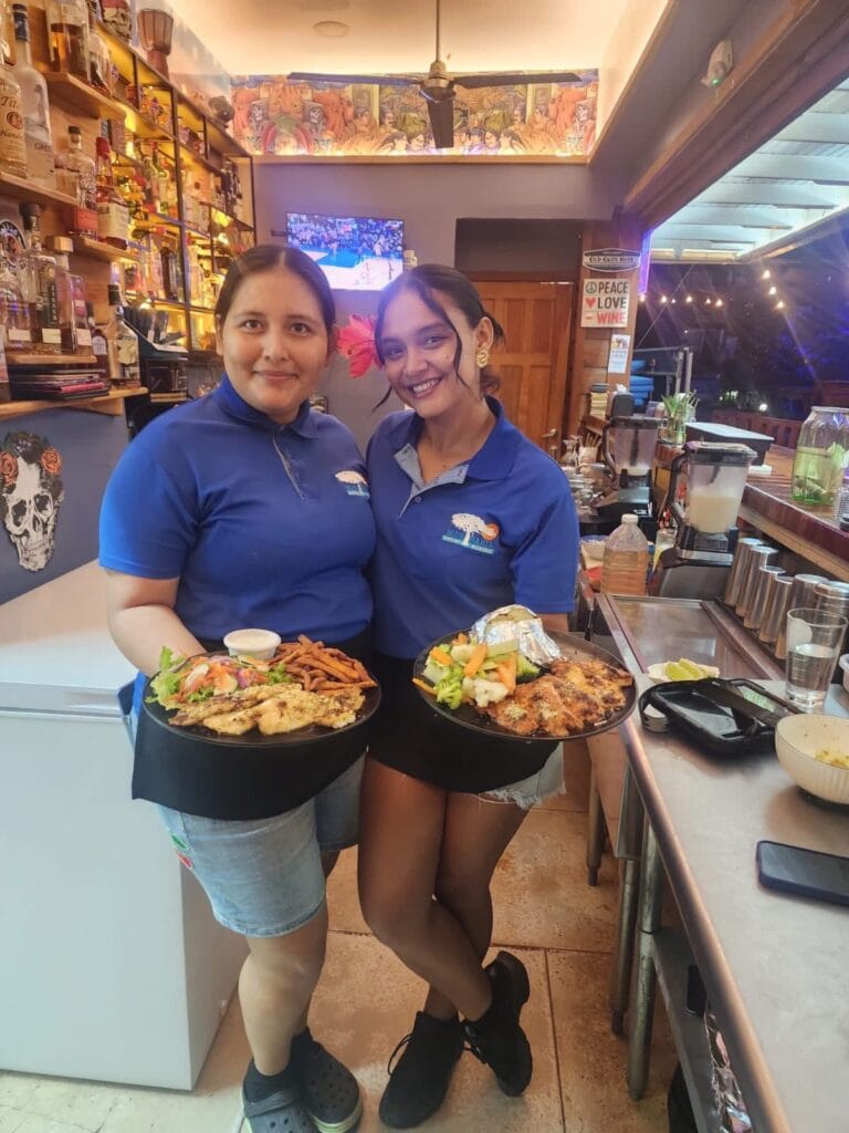 Two smiling waitresses holding plates of food at Blue Bahia Beach Grill.