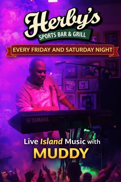A man plays a keyboard on a stage at Herbly's Sports Bar & Grill in Roatan, Honduras, with colorful lighting and promotional signage for live island music with Muddy every Friday and Saturday night.