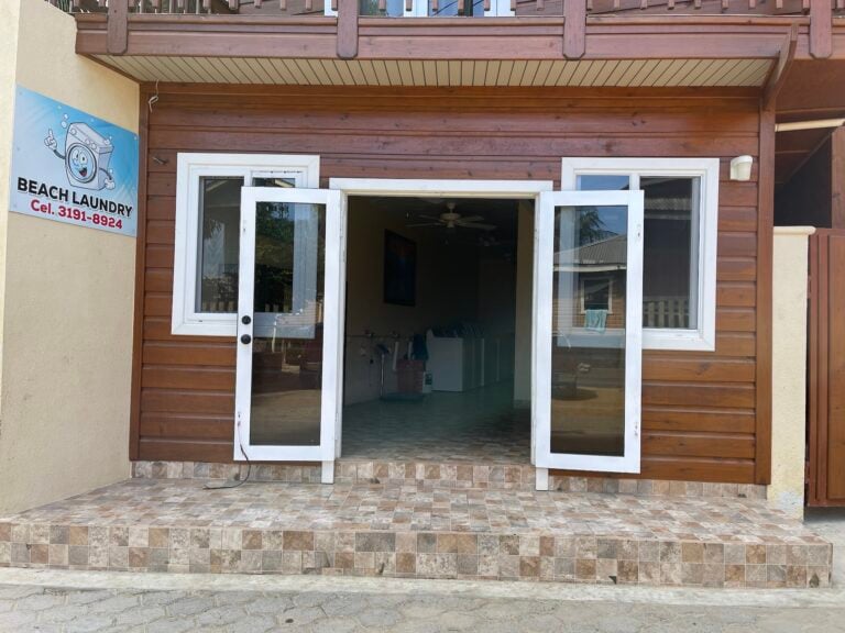 Open doorway to a laundry business on Roatan with wooden exterior and white-framed glass doors, located in Honduras with a tiled concrete step.