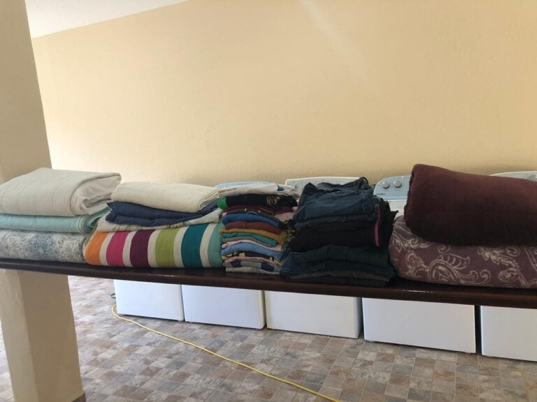 A laundry room on Roatan with folded clothes and towels placed on a dark wooden counter against a beige wall.