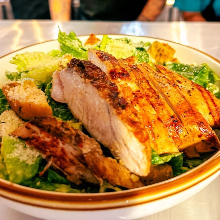 Grilled fish fillet served on a bed of fresh greens with shredded cheese and seasoned vegetables on a white plate in Roatan Honduras.