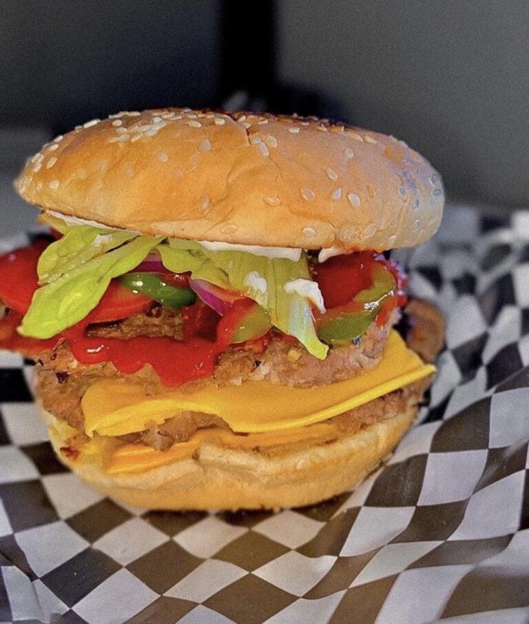 A loaded cheeseburger with a sesame bun, beef patty, melted cheddar, lettuce, tomato, onions, and peppers served in Roatan, Honduras.