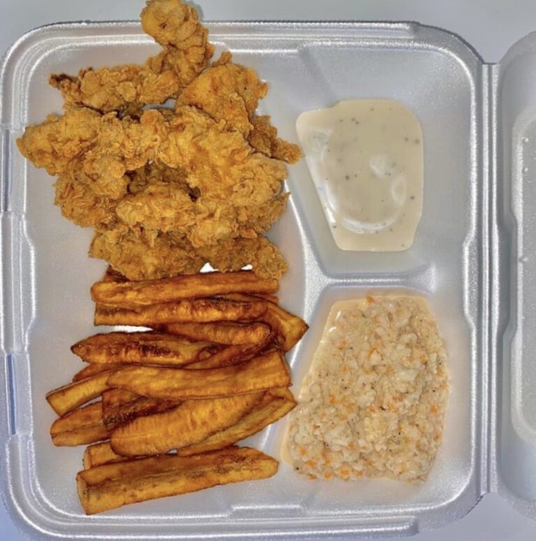 A takeout meal in Roatan, Honduras, features crispy fried chicken, fried plantains, seasoned rice, and creamy dipping sauce.