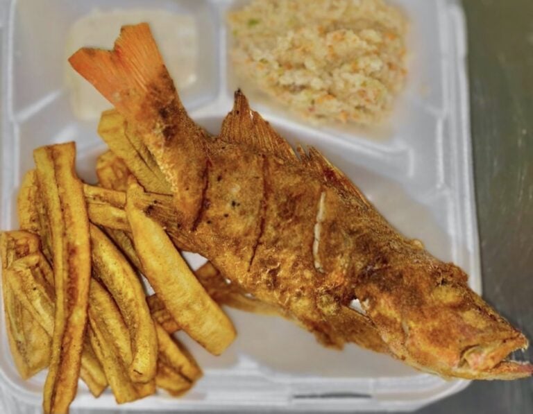 A whole fried fish is served with fried plantains and seasoned rice on a takeout tray in Roatan, Honduras.