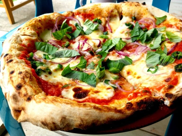 Close-up of a freshly baked pizza topped with melted cheese, fresh basil leaves, red onion slices, and green peppers with a golden, slightly charred crust in a Roatan restaurant setting Honduras.