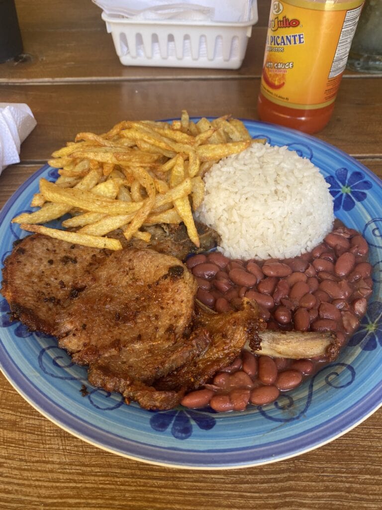 Plate of traditional Honduran food served on a colorful ceramic dish with rice, fried plantains, beans, and a piece of grilled meat, set on a wooden table in Roatan, Honduras.