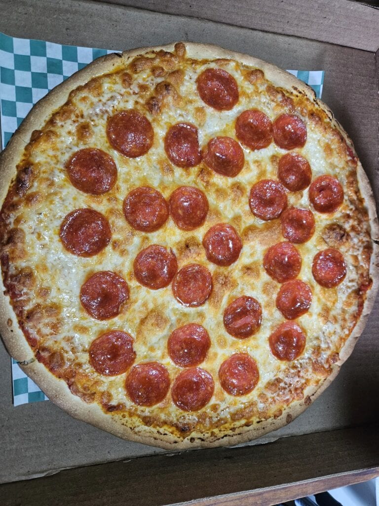 A close-up image of a freshly baked pepperoni pizza with melted cheese on a rustic wooden table, showcasing the vibrant red pepperoni slices and golden crust in Roatan, Honduras.