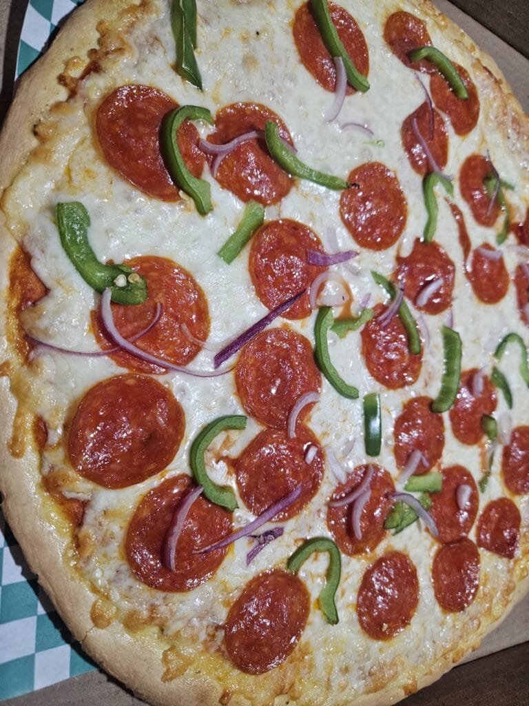 A close-up of a freshly baked pizza topped with pepperoni, green bell peppers, and red onions on a wooden table in Roatan, Honduras.