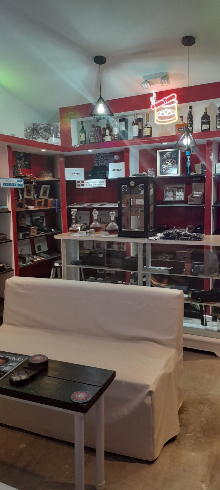 Interior view of a cigar and liquor shop on Roatan, Honduras, featuring shelves with alcohol bottles, a neon sign, and display cases with cigars and accessories.