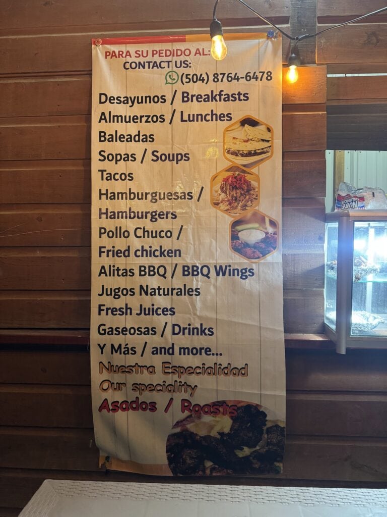 A Spanish-language restaurant menu in Roatan, Honduras lists breakfasts, lunches, tacos, burgers, fried chicken, barbecue wings, fresh juices, drinks, and roasted meats.