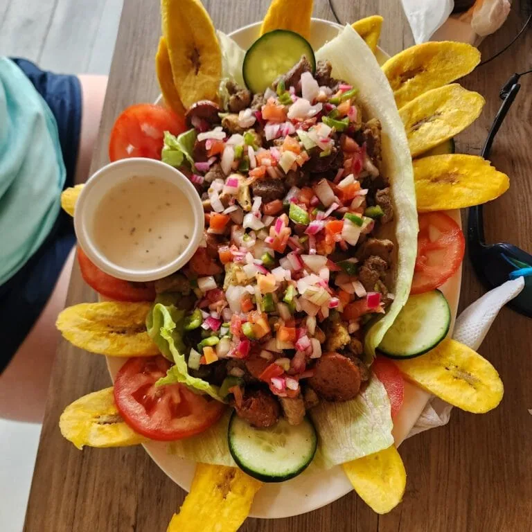 A colorful plate of traditional Honduran baleadas topped with fresh vegetables, crispy plantain chips, and a side of creamy sauce on a wooden table in Roatan, Honduras.