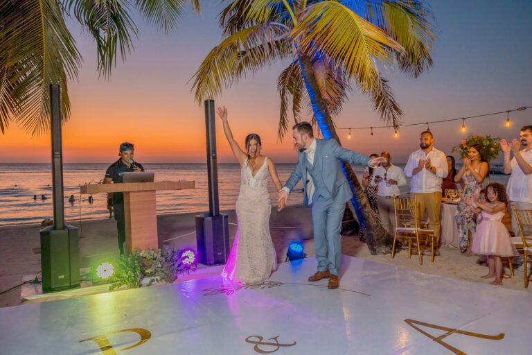 Bride and groom dancing on the beach during sunset celebration.