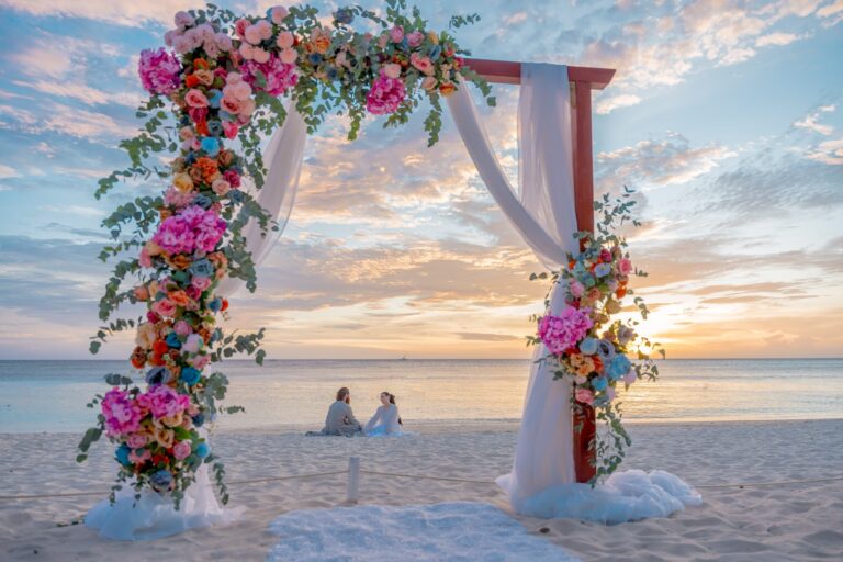 Beach wedding arch decorated with colorful flowers and white drapes.