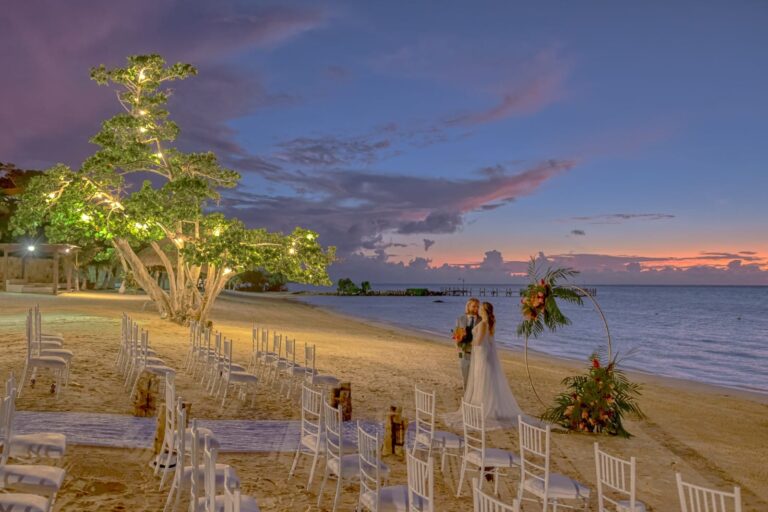Romantic beach wedding setup with chairs, floral arrangements, and ocean view.