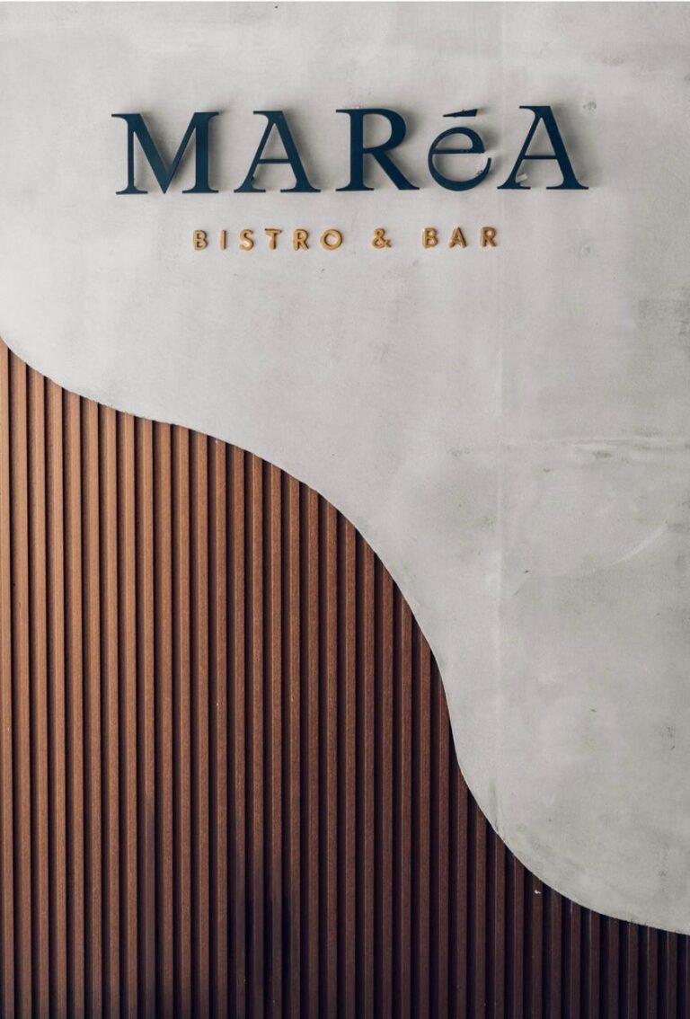 The Marea Bistro & Bar logo appears on a textured wall above curved dark wood paneling in Roatan, Honduras.