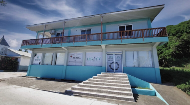 Two-story medical building on Roatan, Bay Islands, Honduras, with blue exterior walls, a staircase leading to glass doors, and signage for Legacy International Mission Center.