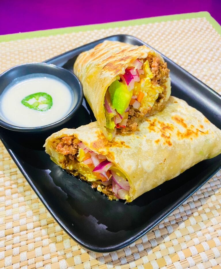 A toasted burrito cut open to show seasoned meat, yellow rice, vegetables, and pink onions beside creamy dipping sauce in Roatan, Honduras.