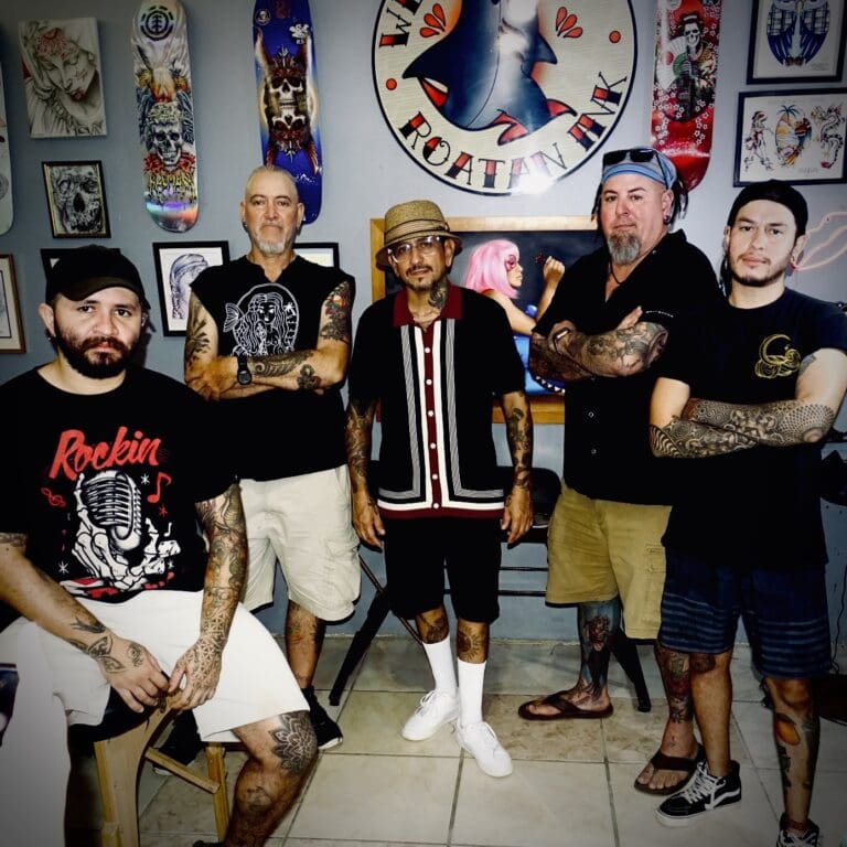 Five tattooed musicians pose together in a colorful art-filled room in Roatan, Honduras.