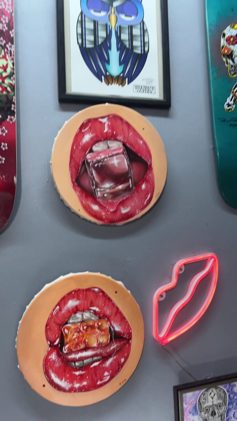 A colorful wall display in Roatan, Honduras features two round red lip artworks, a glowing pink neon lips sign, and a framed blue marine-themed print.