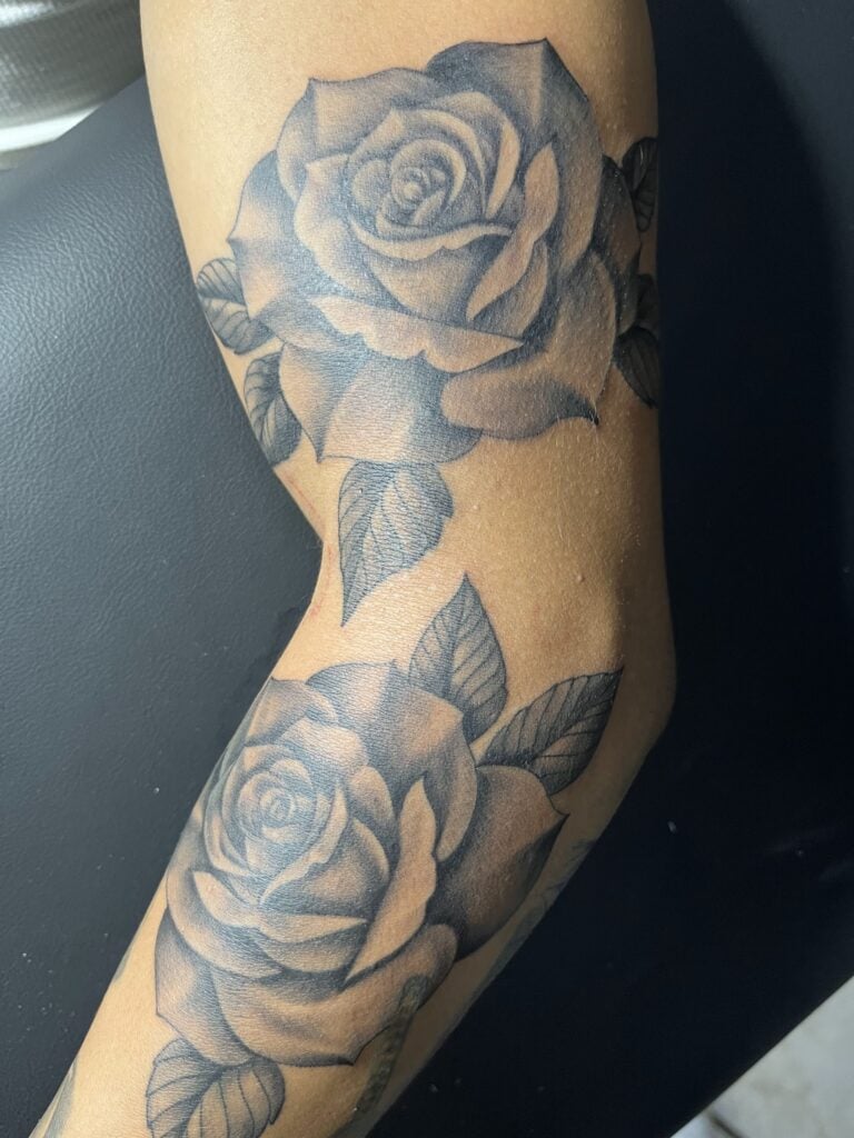 A detailed black and gray rose tattoo with leaves covers a person’s forearm in Roatan, Honduras.