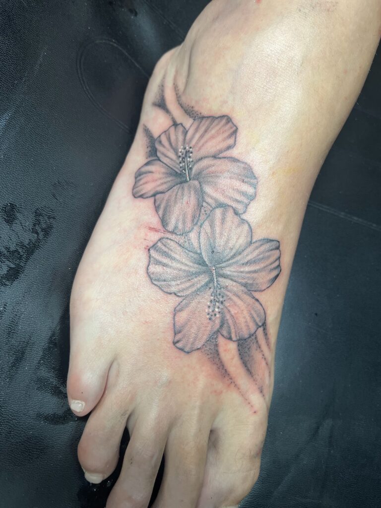 Two hibiscus flowers are tattooed along the top of a person's foot in Roatan, Honduras.