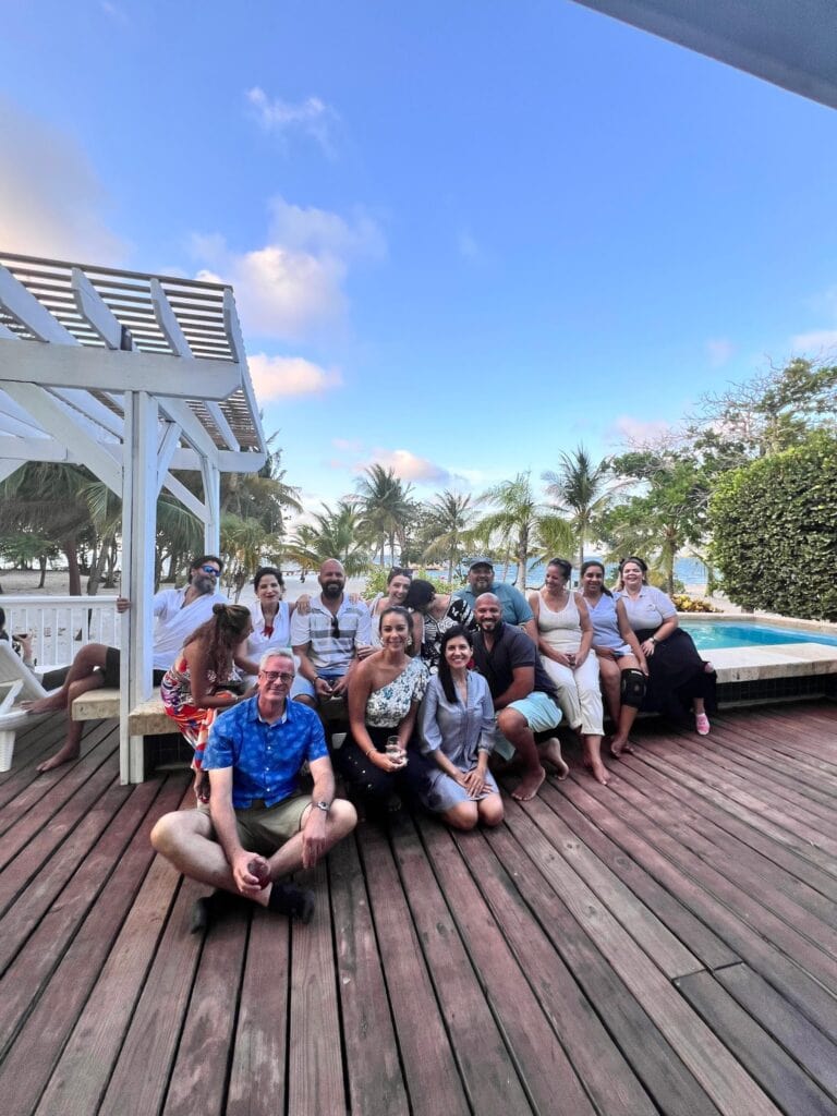 People gathered outdoors near a pool with palm trees and blue sky.