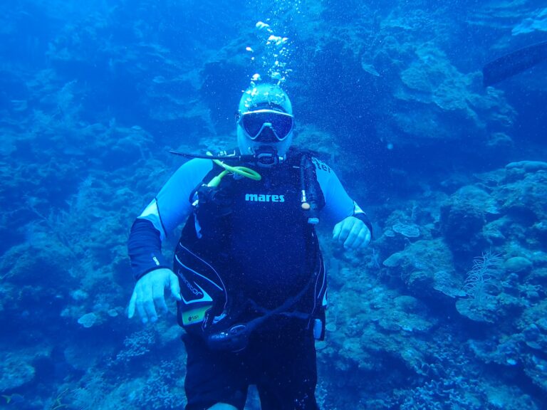A scuba diver with a mask and wetsuit underwater near coral reefs in Roatan, Bay Islands, Honduras, exploring vibrant marine life.