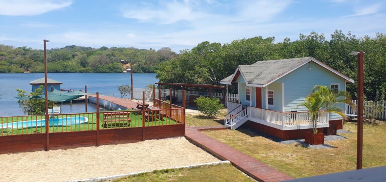 A cozy lakeside cottage in Roatan, Honduras, with a private dock, pool, and lush greenery overlooking the calm waters of the bay.