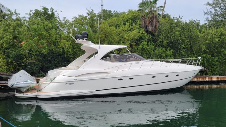A white luxury yacht is docked at a pier with lush green trees and palm trees in the background on Roatan, Honduras.