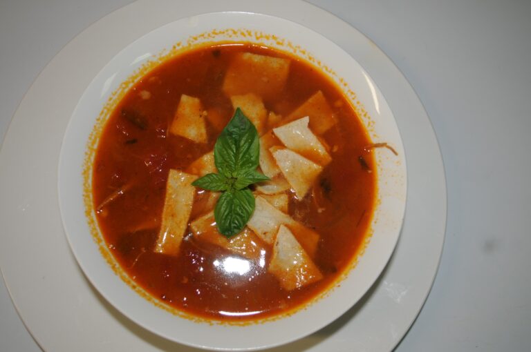 Delicious fish soup with fresh ingredients, served with crispy tortilla chips and a basil garnish.