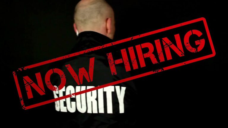 A person wearing a security jacket is seen with a large red "NOW HIRING" stamp across the image, set against a dark background, on Roatan, Honduras.