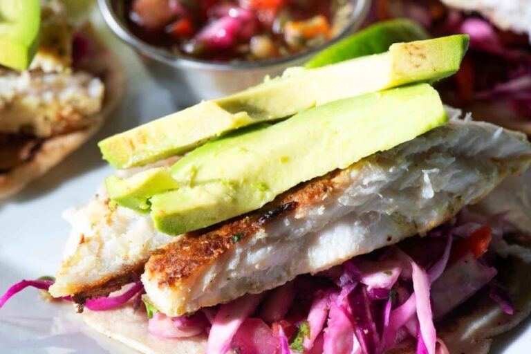 A fresh fish fillet topped with sliced avocado and served on a bun with pickled red cabbage on Roatan, Honduras, highlighting local Caribbean cuisine.