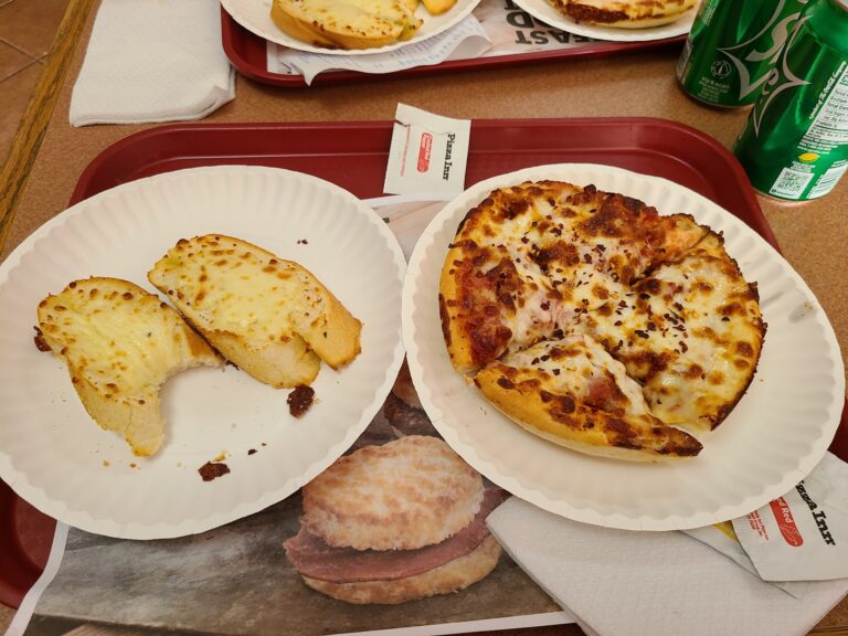 Slices of garlic bread and a cheese pizza on a tray with sodas are displayed on a table at a restaurant in Roatan, Honduras.