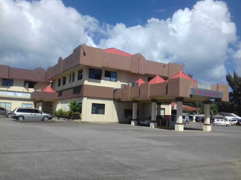 A multi-story commercial building with red rooftop accents and signage for Davivienda bank, located in Roatan, Honduras, is shown in this image under a partly cloudy sky.