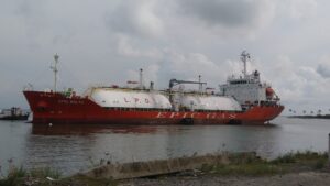 A large red and white LPG gas tanker named "EPIC BALTA" is docked in Roatan, Honduras, with palm trees and a cloudy sky visible in the background.