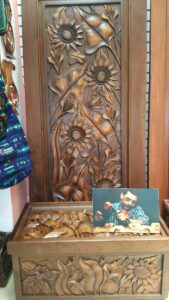 A wooden carved panel featuring sunflowers, leaves, and other floral designs displayed at a business on Roatan, Honduras.
