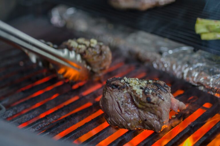 Beef steaks topped with chopped garlic are grilling over an open flame on a barbecue grill in Roatan, Honduras.