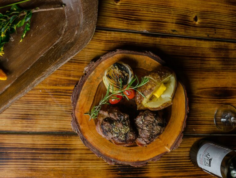 A rustic wooden serving tray on a wooden table in Roatan, Honduras, displays grilled meats, vegetables, and garnishes arranged for a meal.