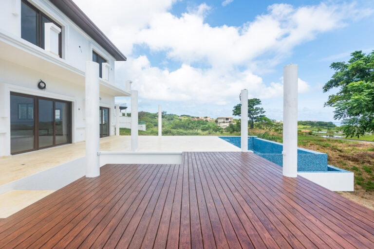 Modern white Caribbean-style villa with a spacious wooden deck and swimming pool overlooking the lush green landscape of Roatan, Honduras.