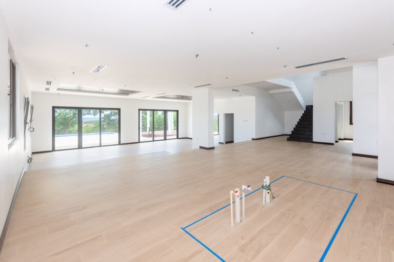 Unfinished interior of a spacious, modern home on Roatan, Honduras with large windows overlooking greenery and a balcony, featuring light wood flooring and white walls.